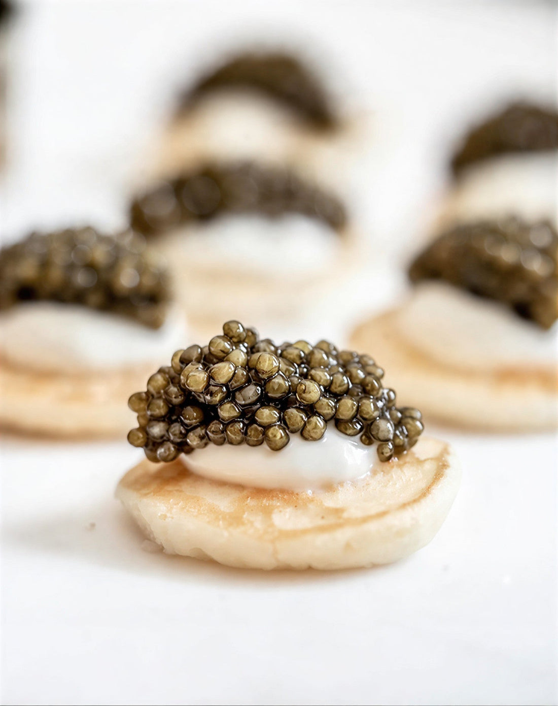 Icre de caviar servite pe blinii mici, cu smântână fină, fotografiate în prim-plan pe fundal alb